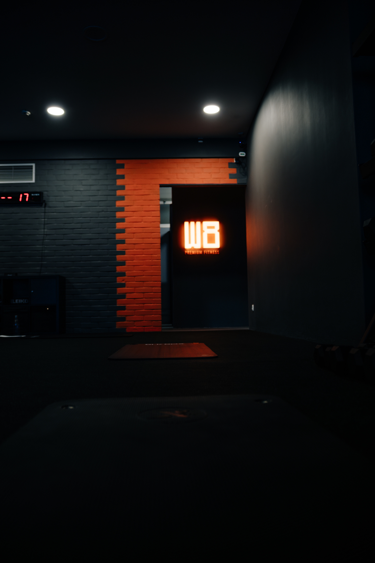 Entrance to W8 Premium Fitness with illuminated logo on black brick wall